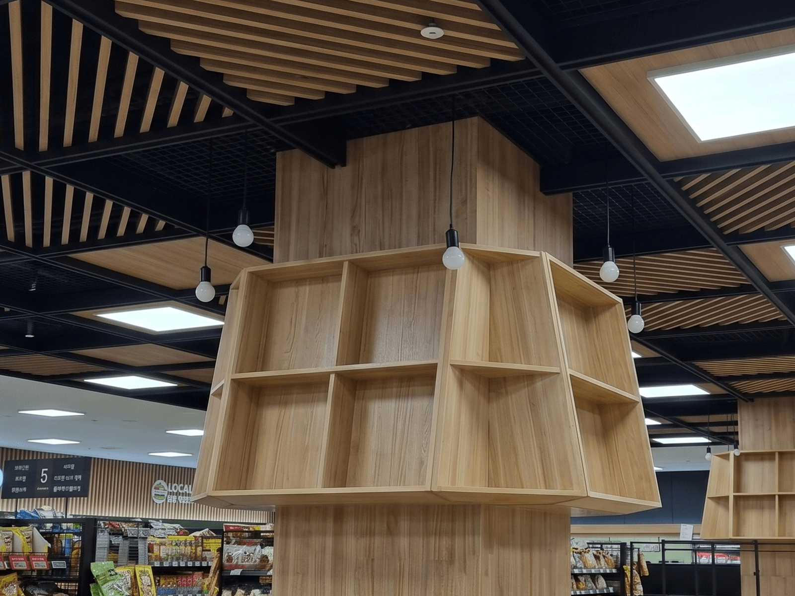 아산 하나로마트 — 시공 전 우드 선반 위로 검은 격자 천장과 펜던트 전구만 있던 빈 상단
