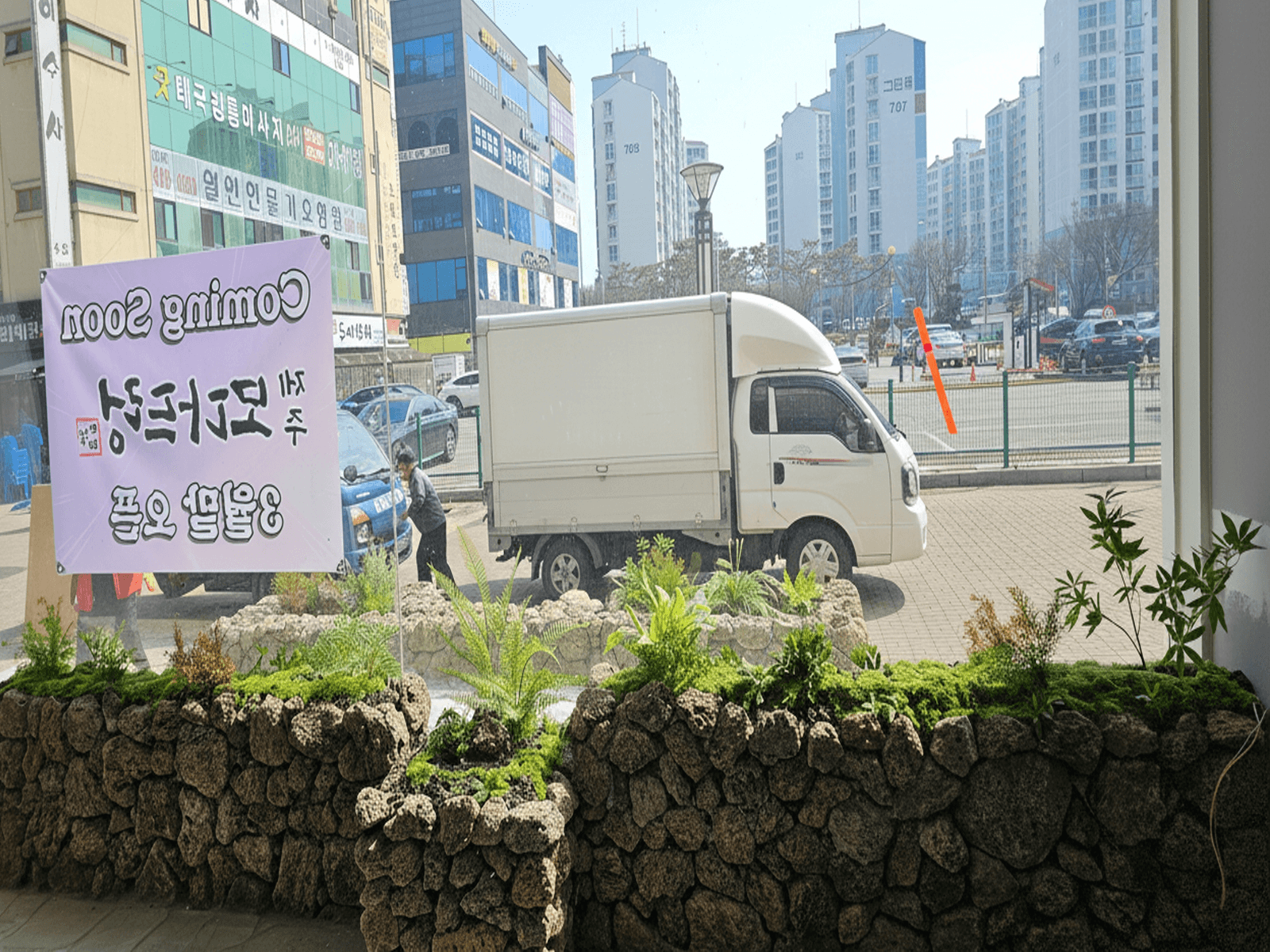 안산 모다드렁 — 매장 안에서 창밖을 볼 때 안쪽 화단 너머 바깥 화단과 거리가 이어져 보이는 장면