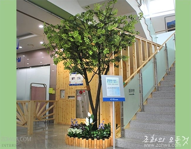 강원 속초병원 — 로비 계단 옆에 시공한 인조 느티나무 한 그루와 그 아래 다채로운 꽃 화단