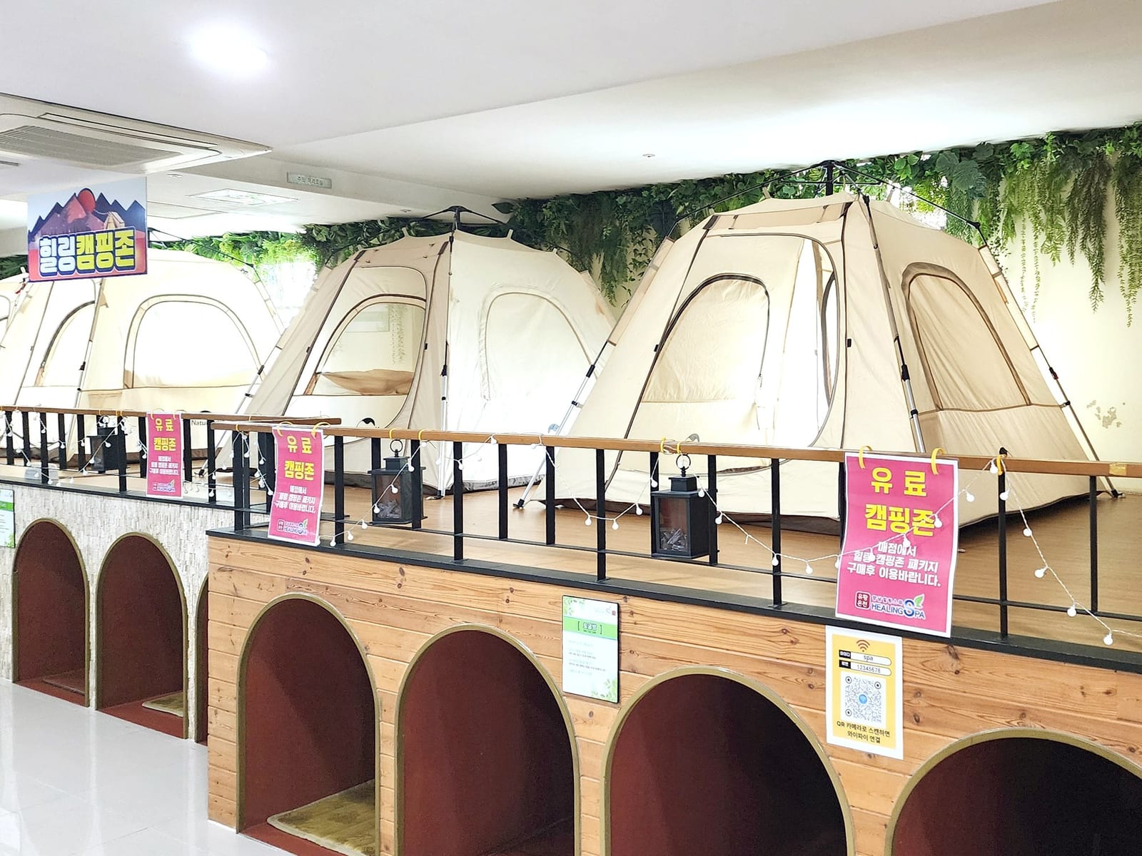 화성 힐링스파 찜질방 — 텐트와 랜턴이 있는 캠핑존을 행잉넝쿨 배경으로 살린 테마 구역 디자인