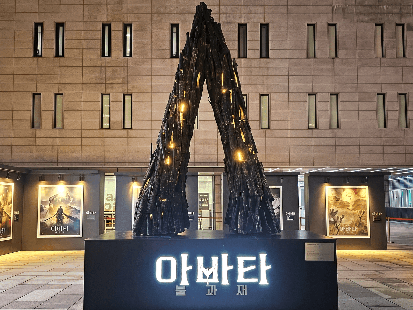 서울 세종문화회관 — 영화 포스터가 늘어선 광장에 세운 거대 A자 행사장 조형물 정면, 밤 조명